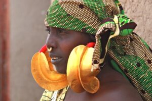 Mopti, Segou and Bamako in 3 Days: Mosques, Markets and City Tour with Niger River Cruise A woman with dark skin is wearing a green, yellow, and black patterned headscarf, large gold earrings, and a nose ring.