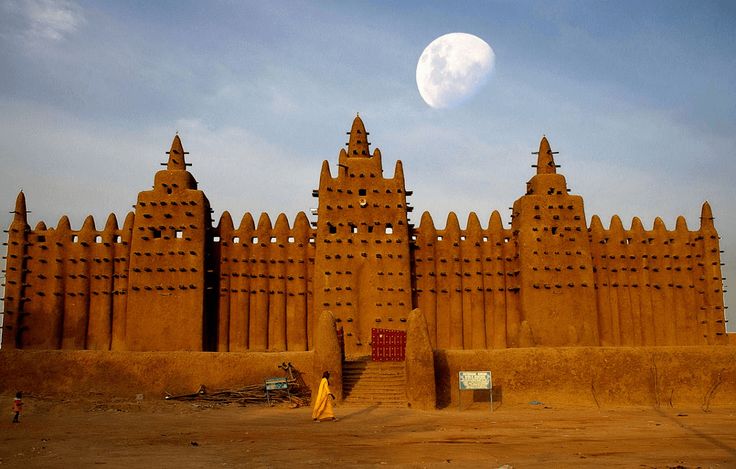 A large mud-brick building stands out in front of a bright moon in the sky.
