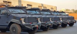 Premium Business Tours: SUV Rentals with Armed Experts in Bamako, Mali A line of black armored vehicles stands in front of a large warehouse, showcasing their robust and imposing design.